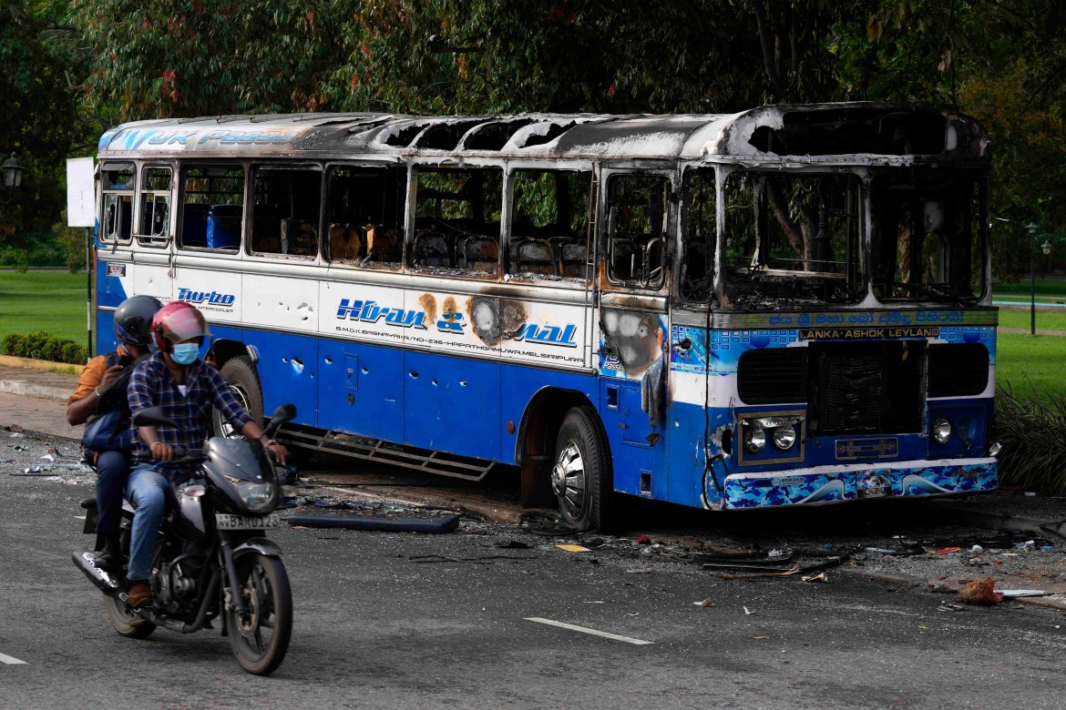 A Sri Lankan motorist rides past a burnt bus a day after clashes between government supporters and anti-government protesters in Colombo