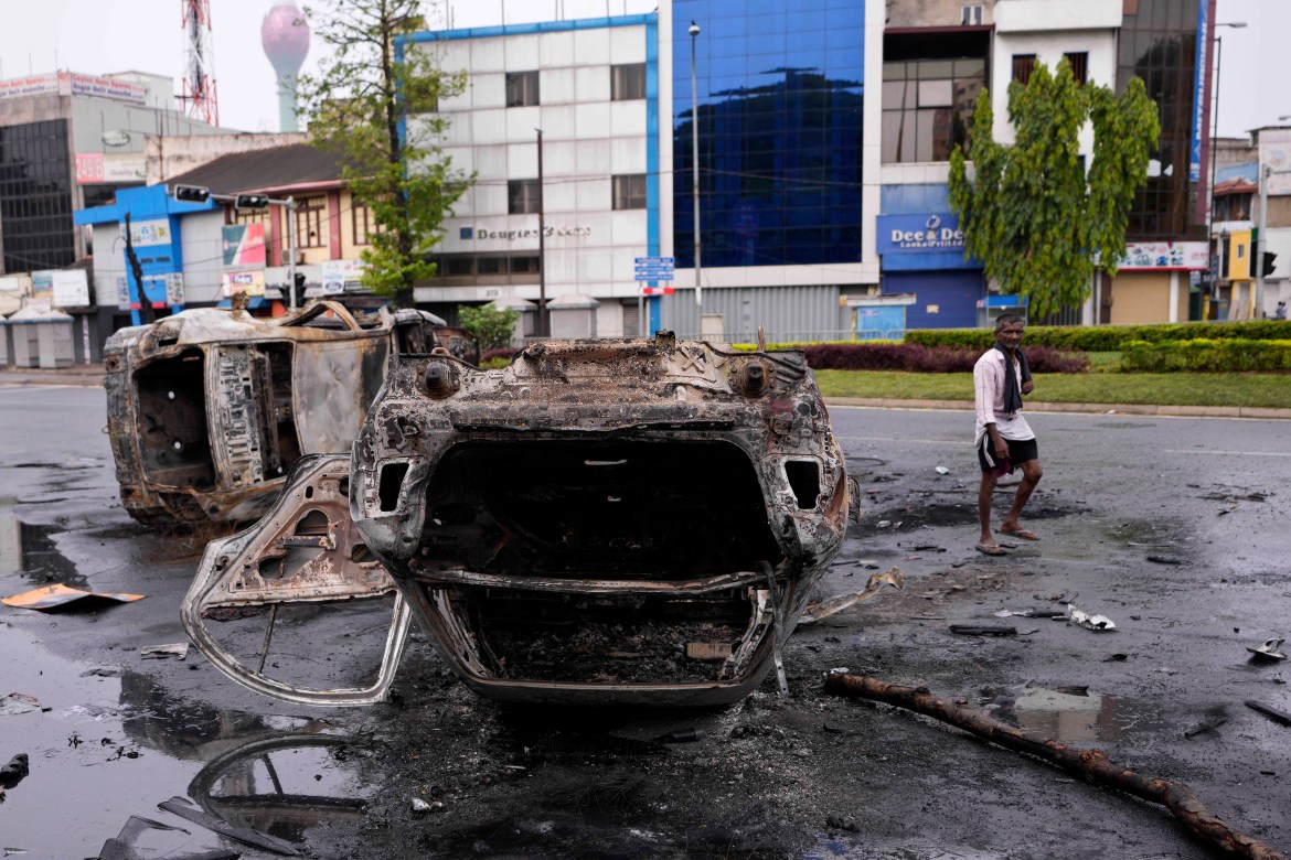 A Sri Lankan man walks past a burnt vehicle a day after clashes between government supporters and anti-government protesters in Colombo