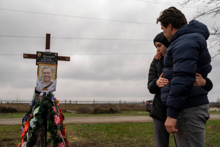 Ukrainians stand near grave of victim at cemetery in Bucha