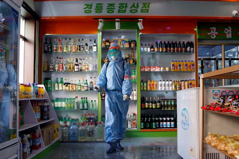 An employee in azmat suit disinfects a food shop in Pyongyang, walking between the aisles with products shown in shelving behind