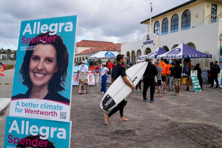A man wearing a wetsuit and surfboard joins the voting line at a polling station in Bondi Beach