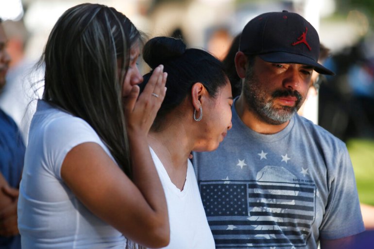 Mario Games, right, and his wife, Marisela and daughter Emily, react as they stand in front of a cross with the name of their niece, Nevaeh Bravo, at a memorial site for the victims killed in this week's elementary school shooting in Uvalde, Texas.