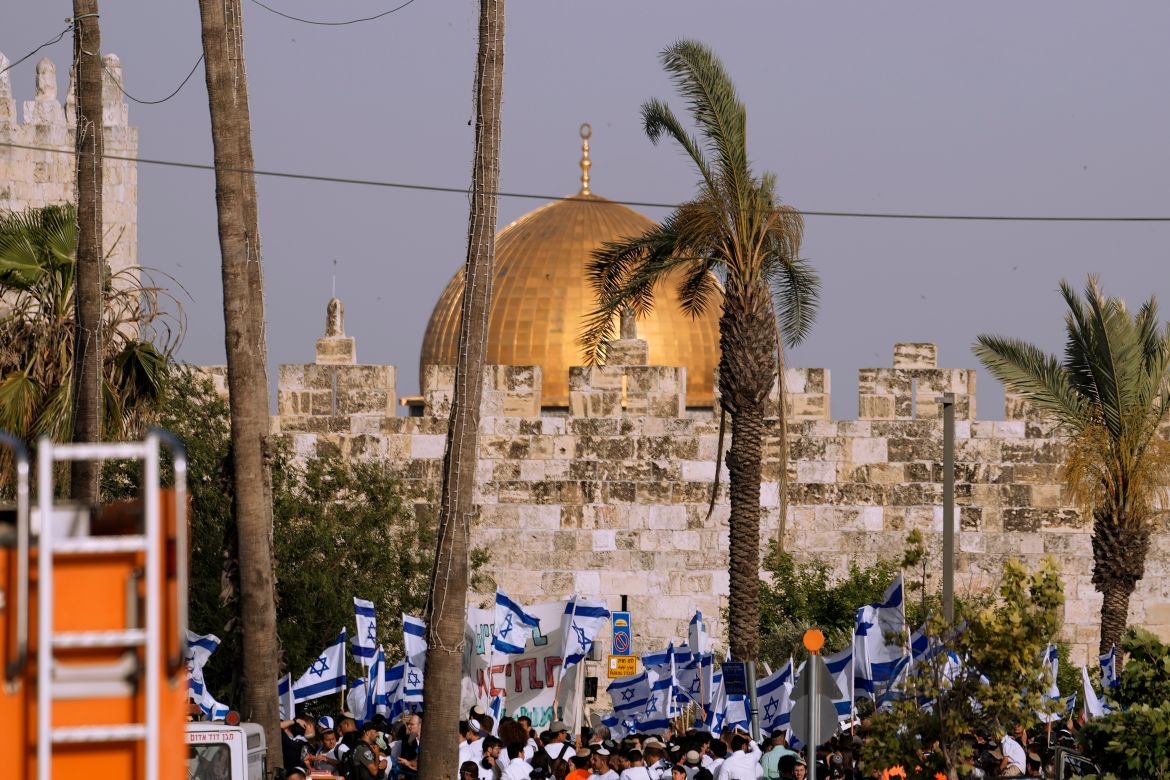 Israelis wave national flags in front of Damascus Gate in occupied East Jerusalem, with the Al-Aqsa Mosque dome showing in the background.