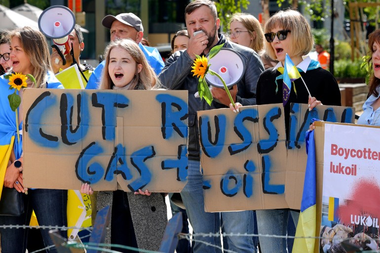 المتظاهرون يطالبون الاتحاد الأوروبي بفرض حظر نفطي خارج القمة حاملين لافتات ويرتدون الأزرق والأصفر - ألوان أوكرانيا.