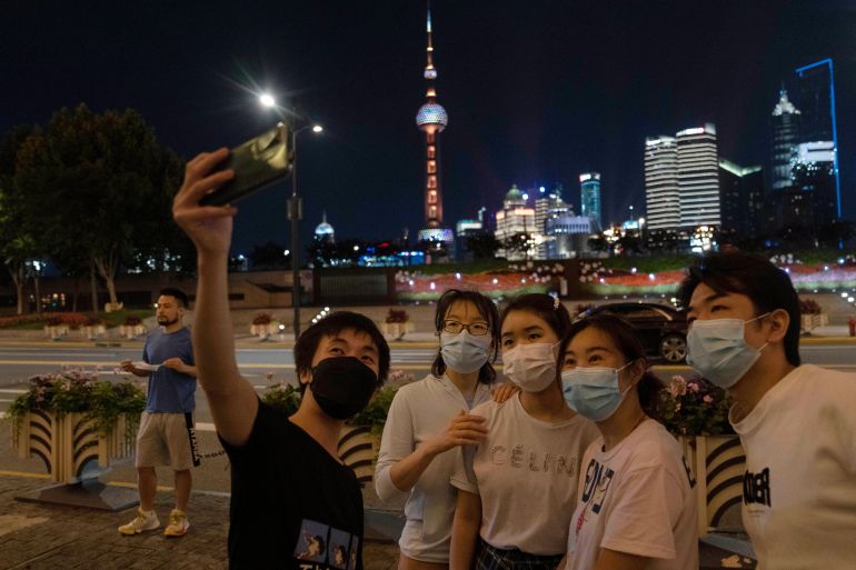 A group takes a night time selfie with the Shanghai skyline behind them as lockdown is eased in the city