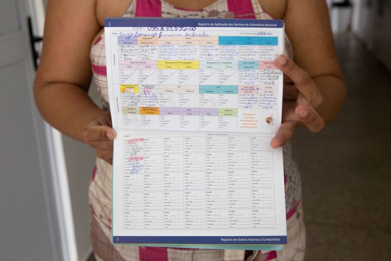 Mother Marlene Ferreira Rosa holds her toddler’s vaccination calendar up after she brought her daughter to a health clinic to get vaccinated against the measles on April 13, 2022 