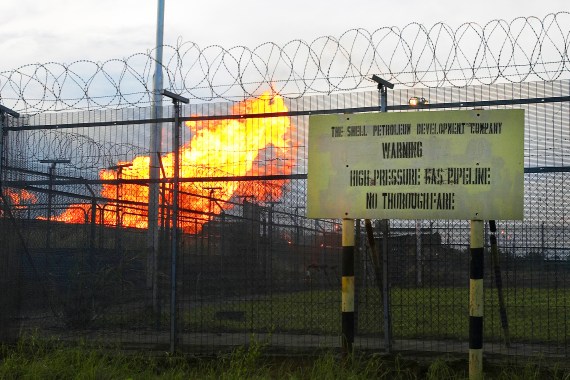 Associated natural gas burns at a flaring site behind a security fence