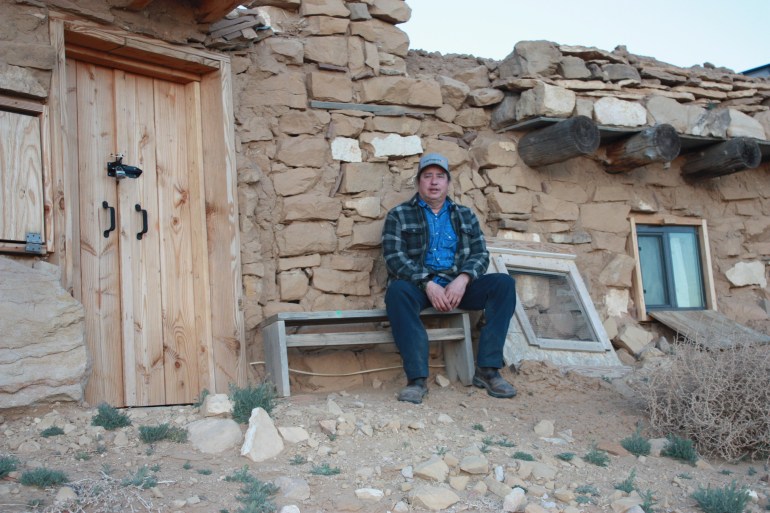 A man sits in front of his stone house