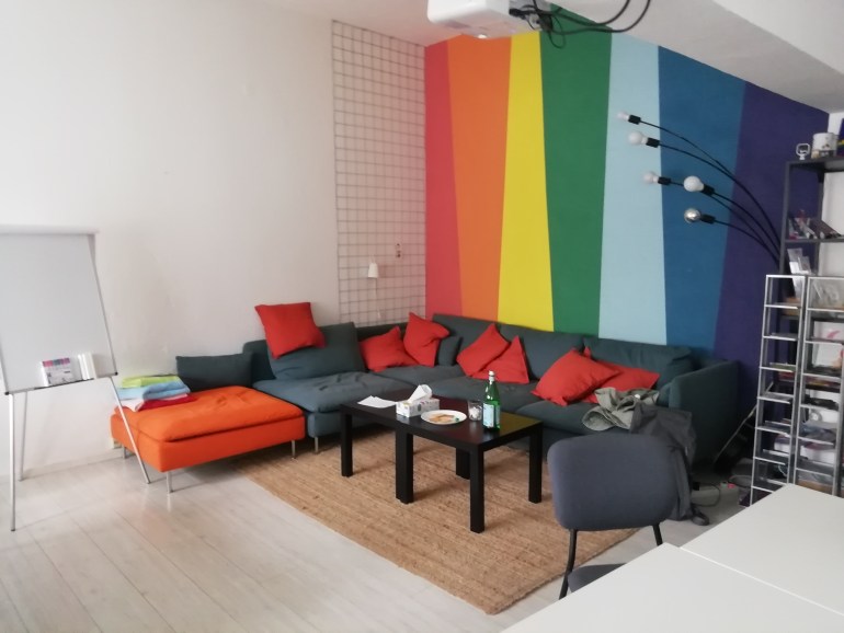 A photo of a room with a sofa and the gay flag is painted on the wall behind the sofa.