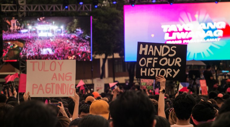 一群年轻人在政治集会上抗议修改历史的努力，他们举着标语牌，上面写着“放开我们的历史”