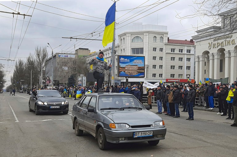 A man stands atop a car with a Ukrainian flag during a rally against the Russian occupation in Svobody (Freedom) Square in Kherson, Ukraine, March 5, 2022