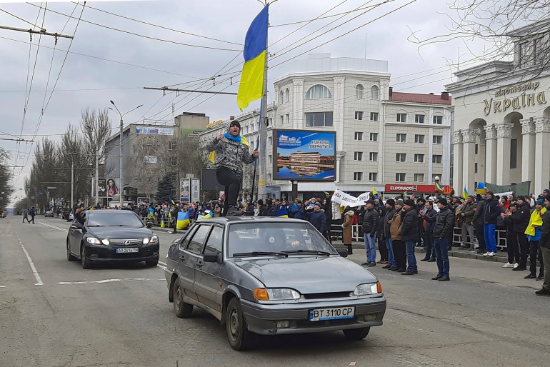 在赫尔松的斯沃博迪（自由）广场举行的反对俄罗斯占领的集会中，一名男子站在一辆挂着乌克兰国旗的汽车顶上。