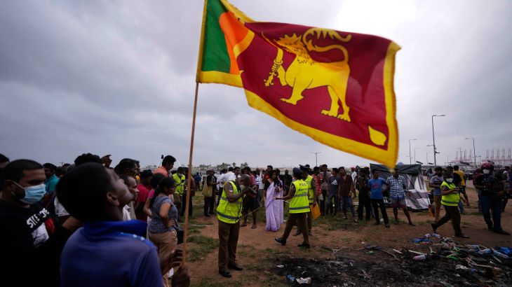A Sri Lankan man holds a national flag as police officers conduct investigations into aftermath of clashes between government supporters and anti government protesters in Colombo, Sri Lanka on May 10.