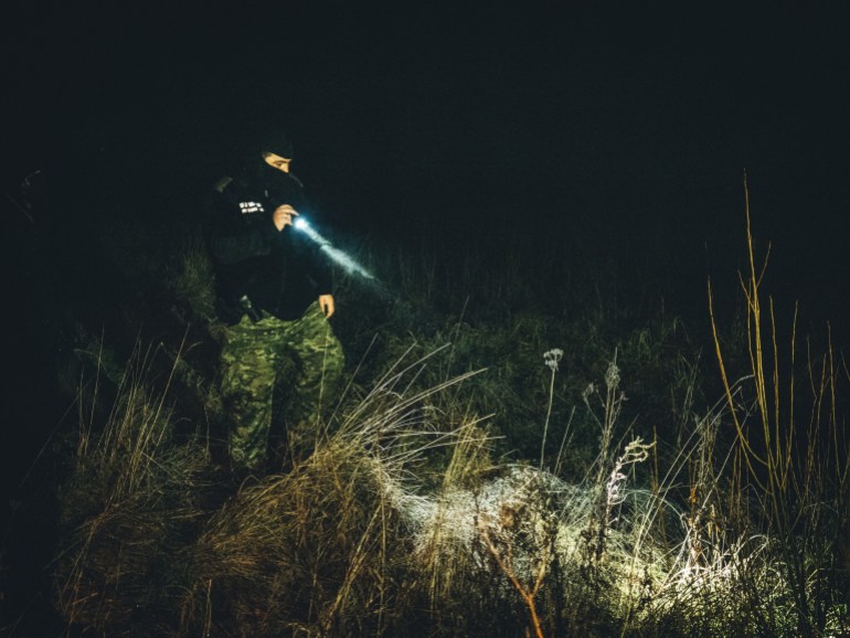 A photo of a Polish border guard using a flashlight at night.