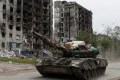 Service members of pro-Russian troops drive a tank past destroyed residential buildings in the town of Popasna in the Luhansk Region
