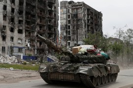 Pro-Russian troops drive a tank past destroyed residential buildings in the town of Popasna in the Luhansk Region, Ukraine, on May 26, 2022 [Alexander Ermochenko/Reuters]