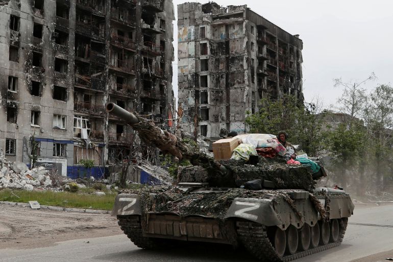 Service members of pro-Russian troops drive a tank past destroyed residential buildings in the town of Popasna in the Luhansk Region