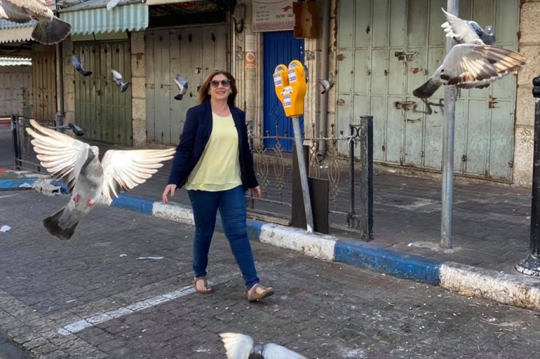Shireen Abu Akleh walking down a street with a pigeon in flight close to her.