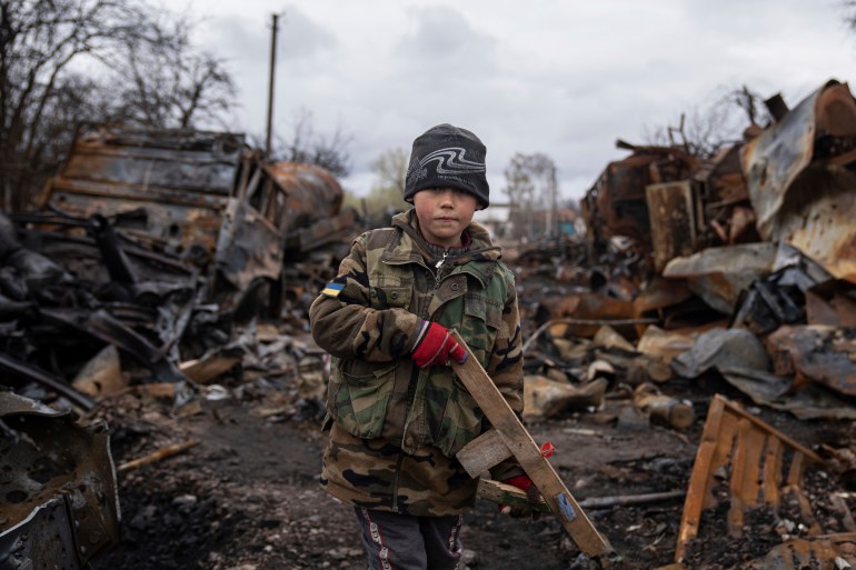 Yehor, 7, stands holding a wooden toy rifle next to destroyed Russian military vehicles near Chernihiv.