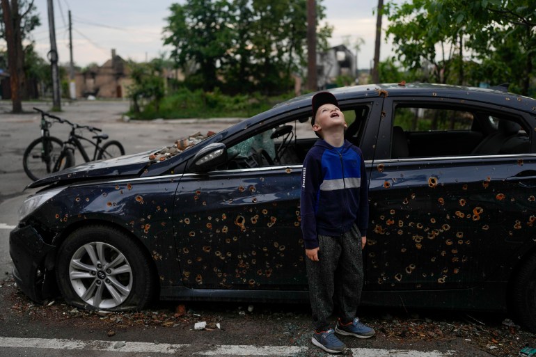 A child standing next to a damaged car looks up at a building destroyed during attacks in Irpin, on the outskirts Kyiv, Ukraine, Monday, May 30, 2022