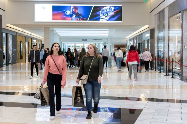 People carrying shopping bags walk inside a shopping mall.