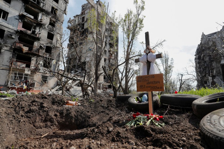 A grave, in front of destroyed apartment blocks, of a civilian killed in the southern port city of Mariupol. Grave board reads: 'Kolesnikov Anatoly Ivanovich', 1957.04.08 - 2022.10.03