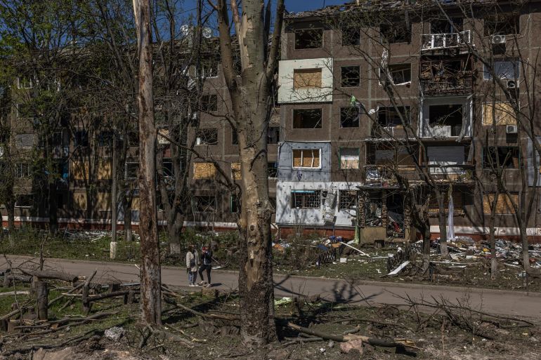 Women stand in front of a bombed out block of flats and blackened trees in Kramatorsk after a Russian air attack