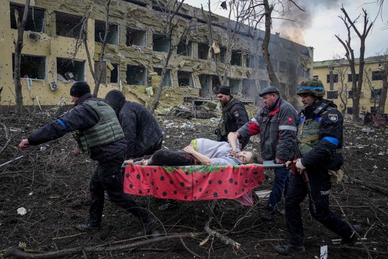 Ukrainian emergency employees and volunteers carry an injured pregnant woman from a maternity hospital damaged by shelling in Mariupol