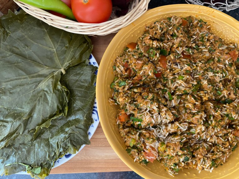 A bowl of rice mixed with spiced mince sits ready to roll up in a pile of grape leaves also seen in photo