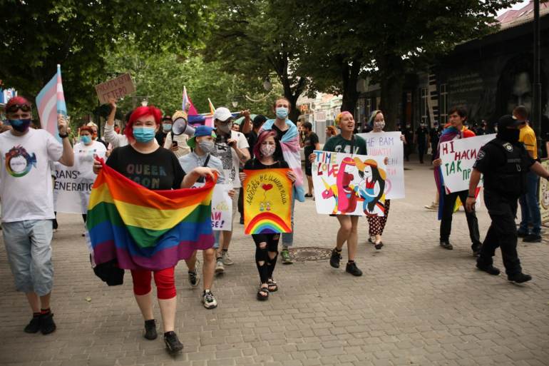 A photo of a large group of people walking and holding vqrious LGBTQA+ posters and flags.