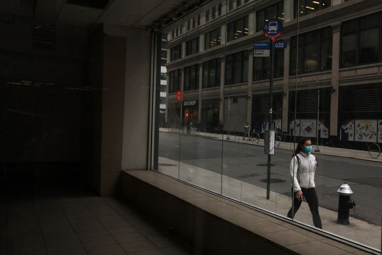 A woman wearing a protective face mask walks past empty commercial real estate in the Midtown Manhattan area of New York City, U.S.
