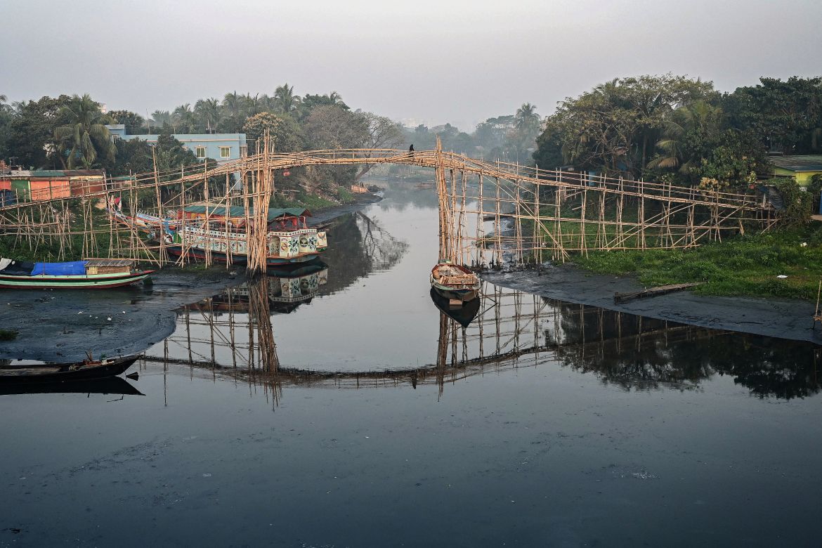 In this picture taken on March 3, 2022, a woman crosses a bamboo bridge over a polluted canal that leads to the Balu River in Dhaka.