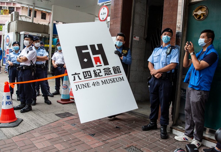 Police officers stand guard on the street as another officer carries out a placard with the numbers 6-4 as the authorities shut down Hong Kong's Tiananmen museum