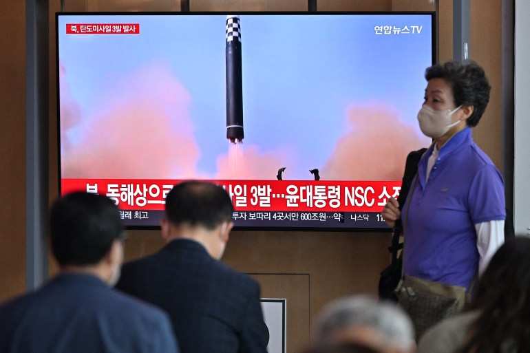 People watch a television screen showing a news broadcast with file footage of a North Korean missile test, at a railway station in Seoul on May 25, 2022
