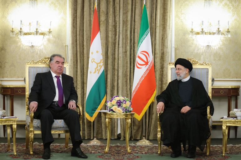 The presidents of Tajikistan and Iran sit in chairs next to each other with the flags of their respective countries