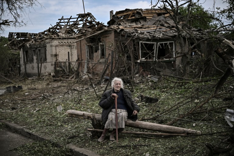 An eldery woman sits in front of destroyed houses after a missile strike