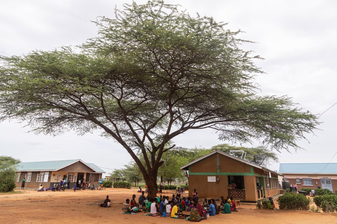 Mothers and their children sit under a tree during a nutrition screening at Nadunget Health Centre