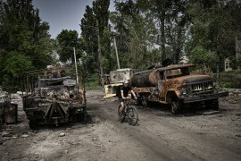 A man rides his bicycle between two destroyed military trucks in the city of Lysychansk, Ukraine.