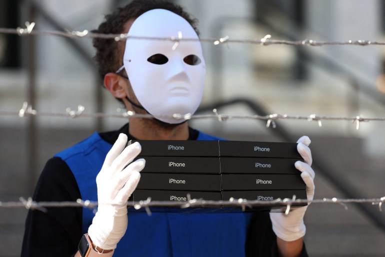 An activist holds a stack of iPhone boxes as he wears a costume depicting Uighurs in a forced labor camp on March 04, 2022 in Washington, DC [File: Justin Sullivan/Getty Images/AFP]