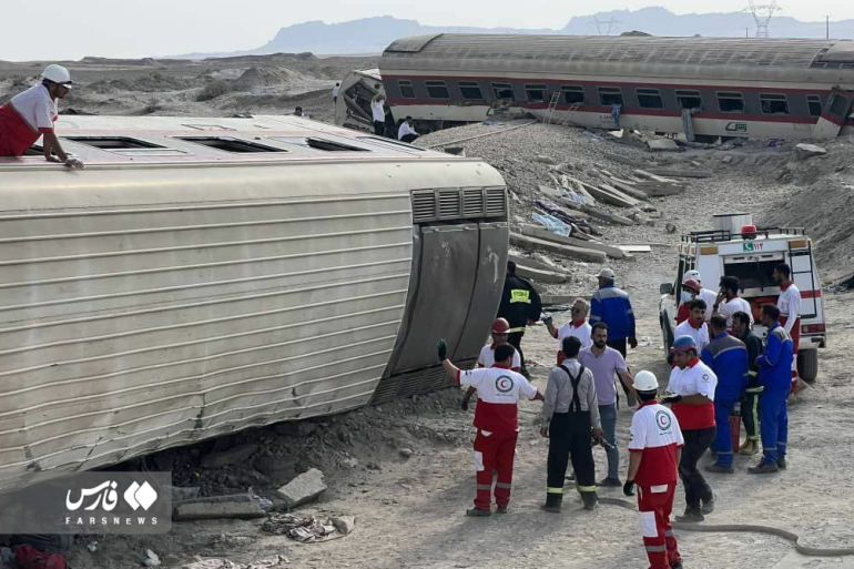 A group of people stand next to a derailed train