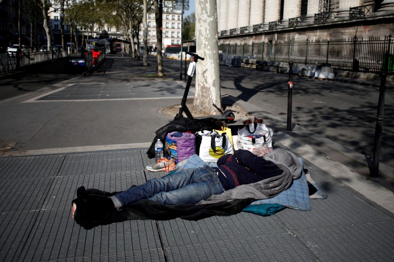 A homeless man sleeps on a metro ventilation shaft near La Madeleine church in Paris
