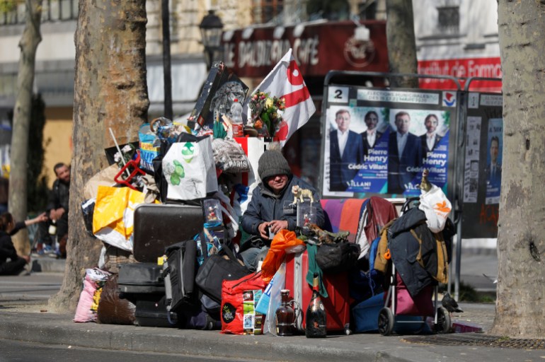 Paris'te bir sokakta eşyalarıyla birlikte oturan evsiz bir kişi. 
