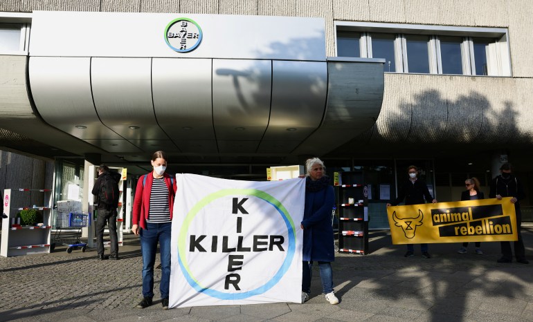 Protesters holding up a sign saying "Killer" in the same pattern as Bayer's logo