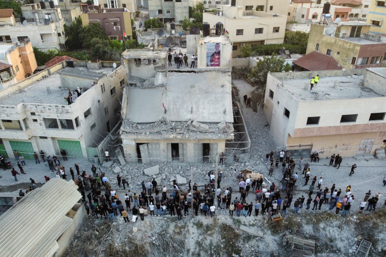A photo of people taken from above as they gather on the street around a destroyed building