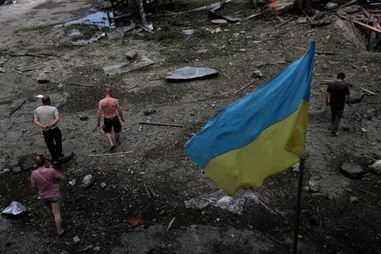 People walk through the remains of a timber warehouse that was bombed near Kharkiv as a Ukrainian flag flies above