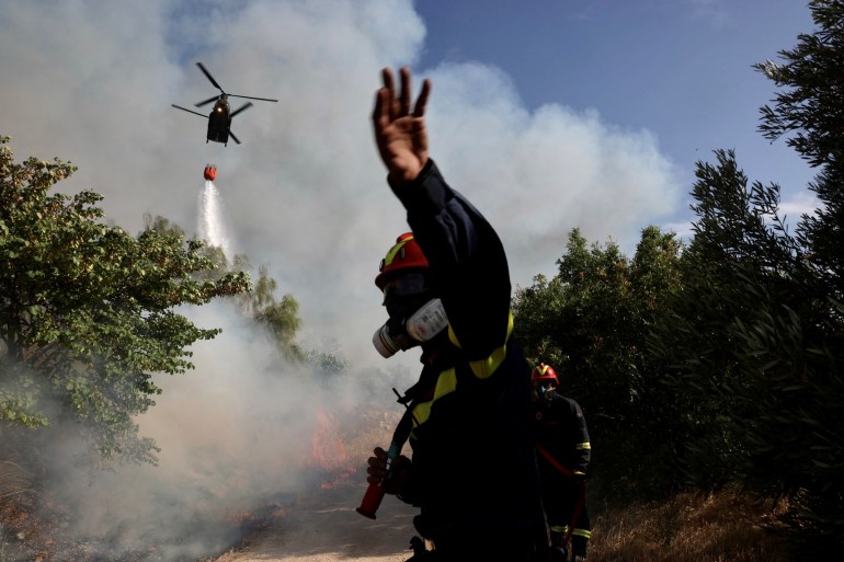A firefighter reacts as a helicopter makes a water drop during a wildfire raging in the suburb of Ano Voula in Athens, Greece, June 4, 2022 [Giorgos Moutafis/Reuters]