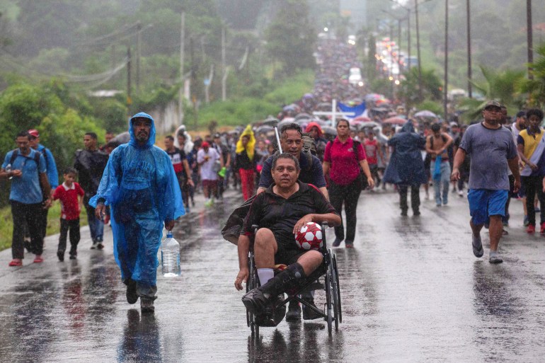 A man in a wheelchair is pushed in a caravan bound for the US