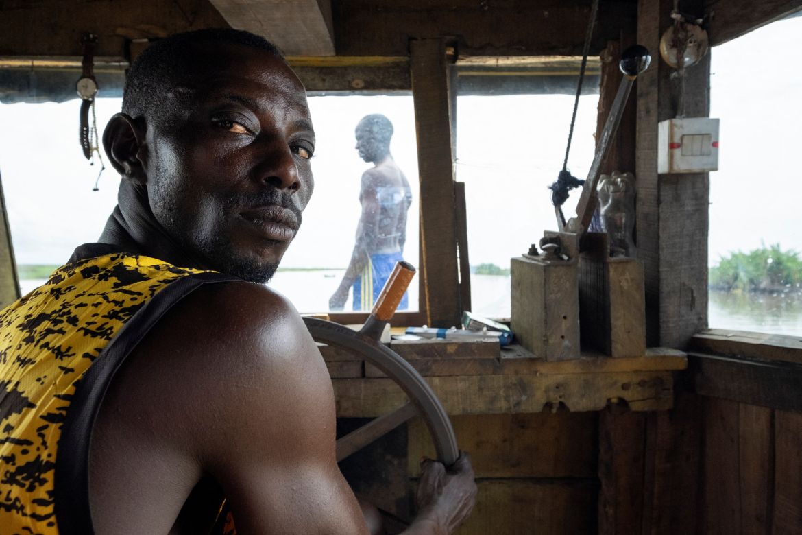 Sunday poses for a photograph, while the captain of the tug boat, Elewuro, is seen through the window, as they set out on their journey to Lagos from Ipare, Ondo State, Nigeria