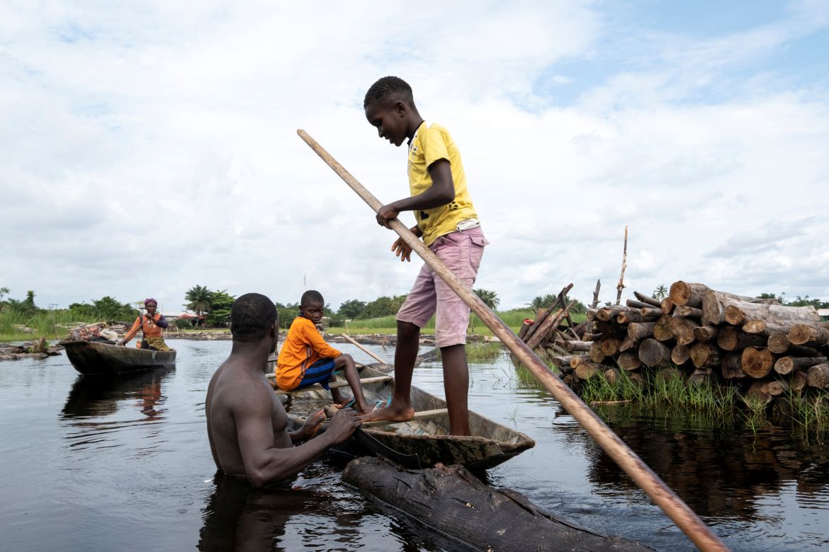 Logger, Komiyo Ikuejamoye, talks with some locals as he pulls his logs through the river in Ipare, Ondo State