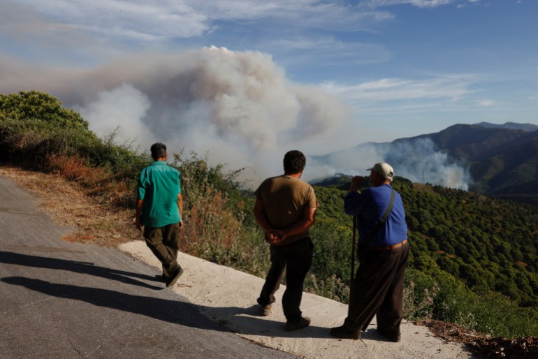 People watch as smoke billows, as a forest fire breaks out in Pujerra,